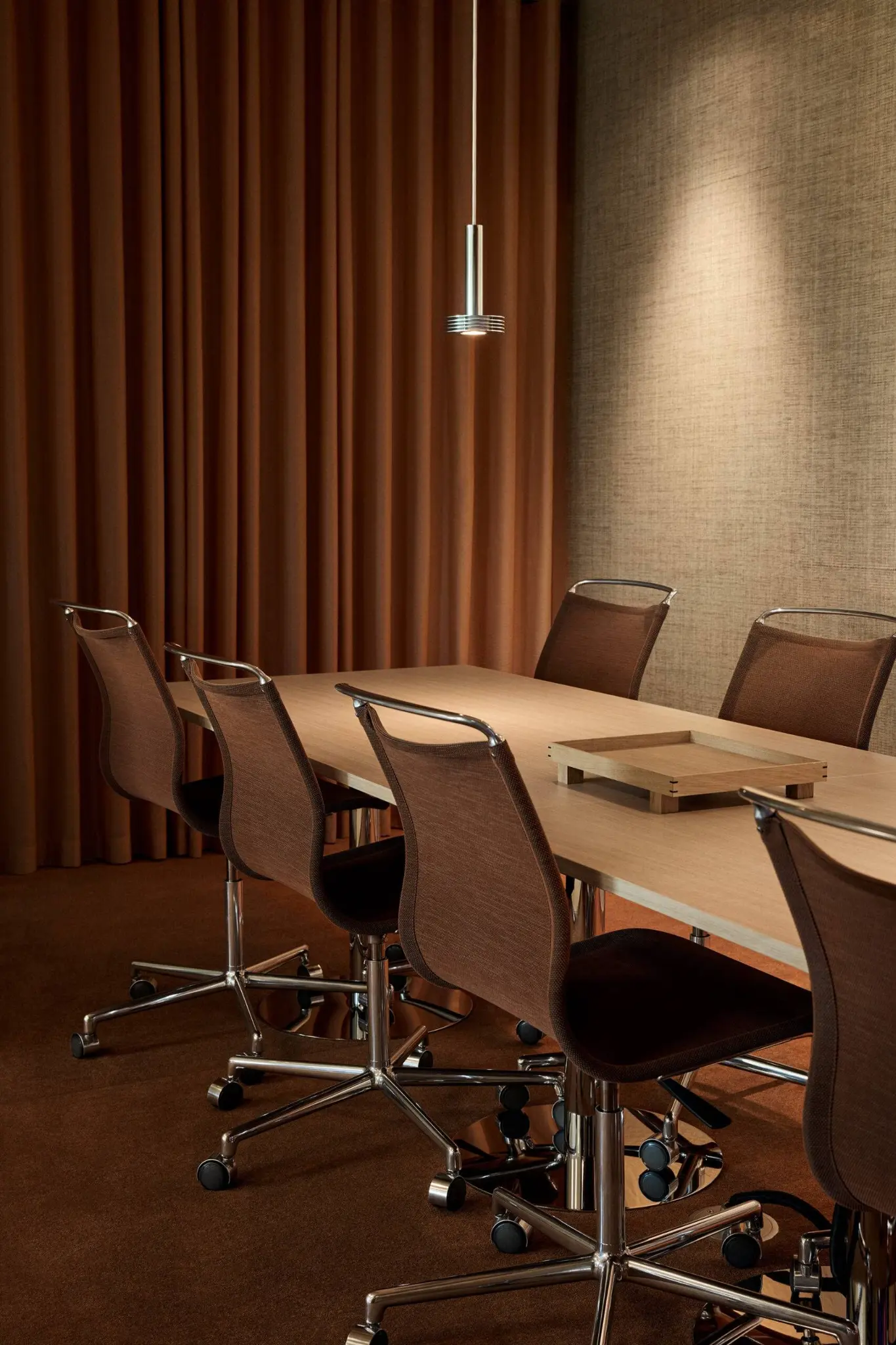 Modern conference room with mesh chairs around a light wood table and a pendant light.