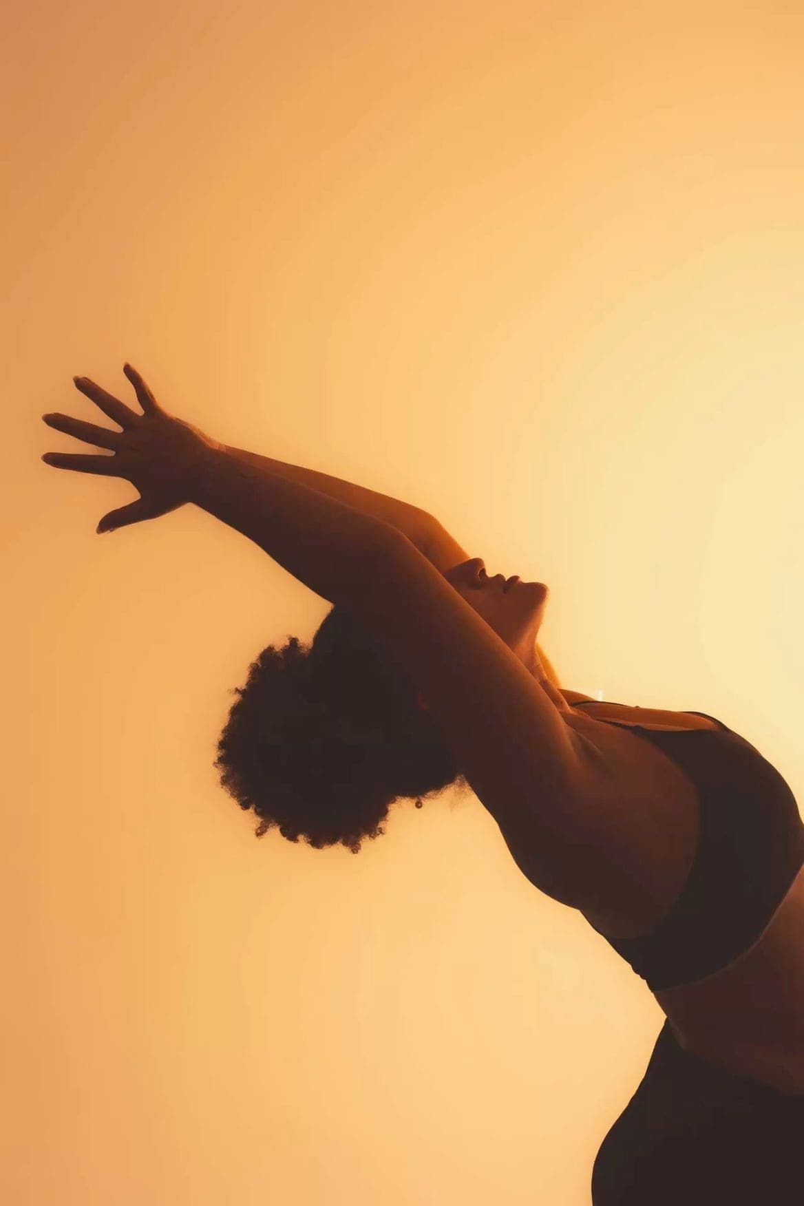 A dancer arched backwards, silhouetted against a glowing amber wall.