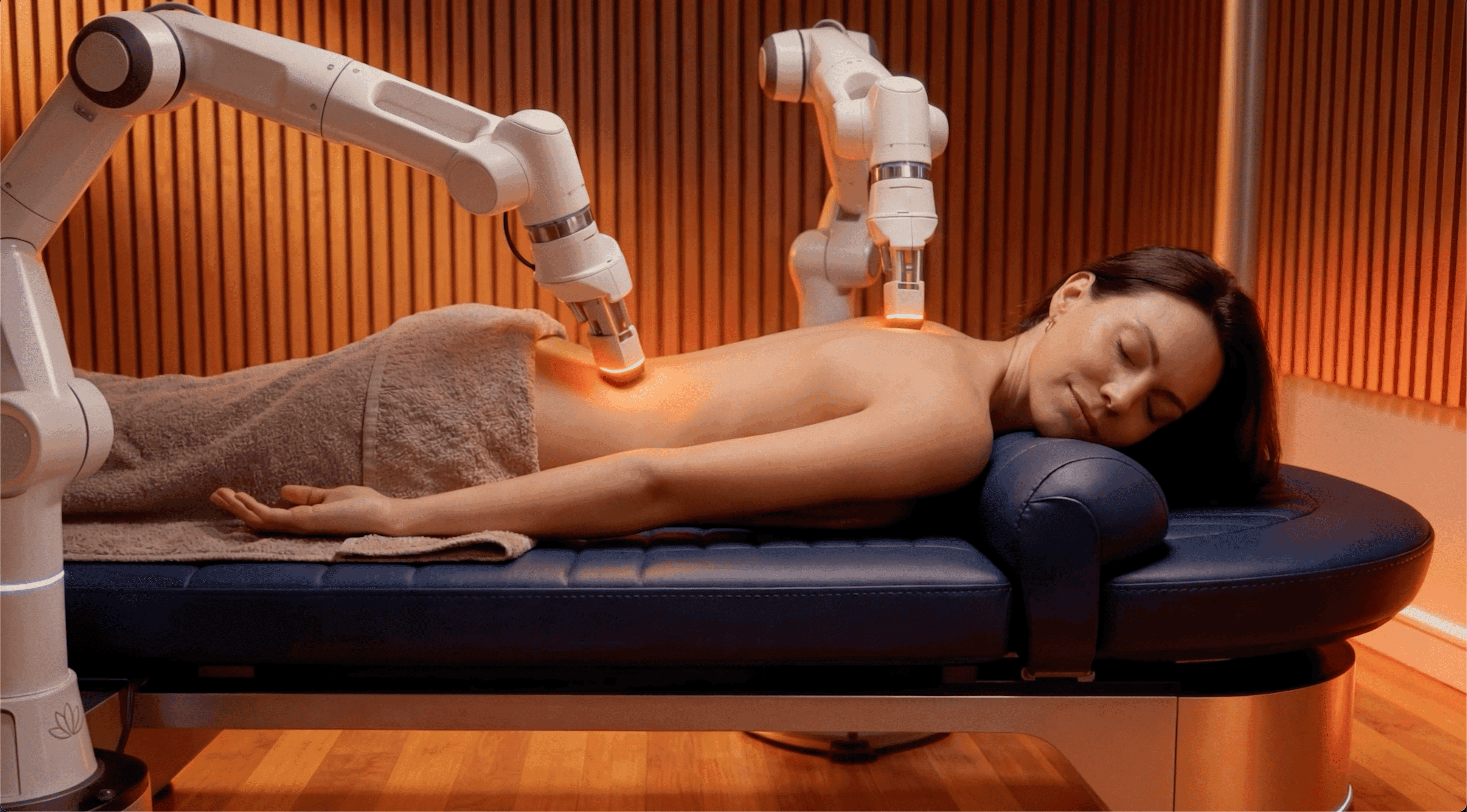 A robotic massage arm working over a person lying face down on a padded treatment bed.